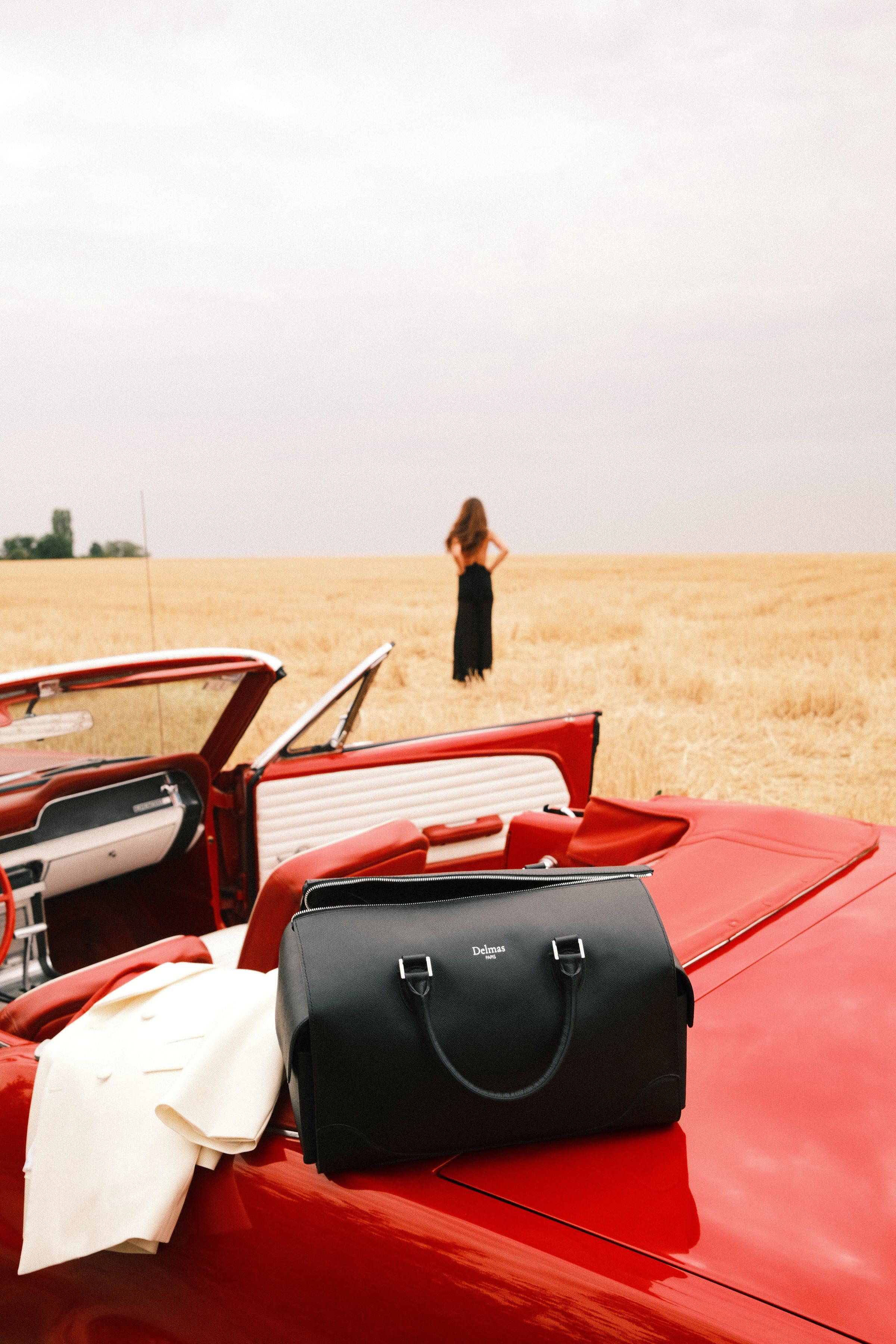 Le Baisenville noir posé sur le coffre d'une Mustang rouge, au bord d'un champ de blé.